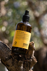 Oway Sea Salt Spray bottle resting on bark with foliage in the background