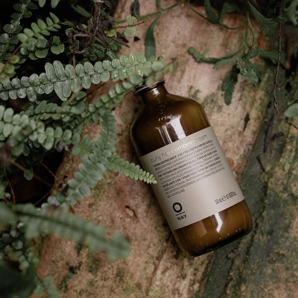Oway Curly Hair Combing Cream bottle photographed among ferns