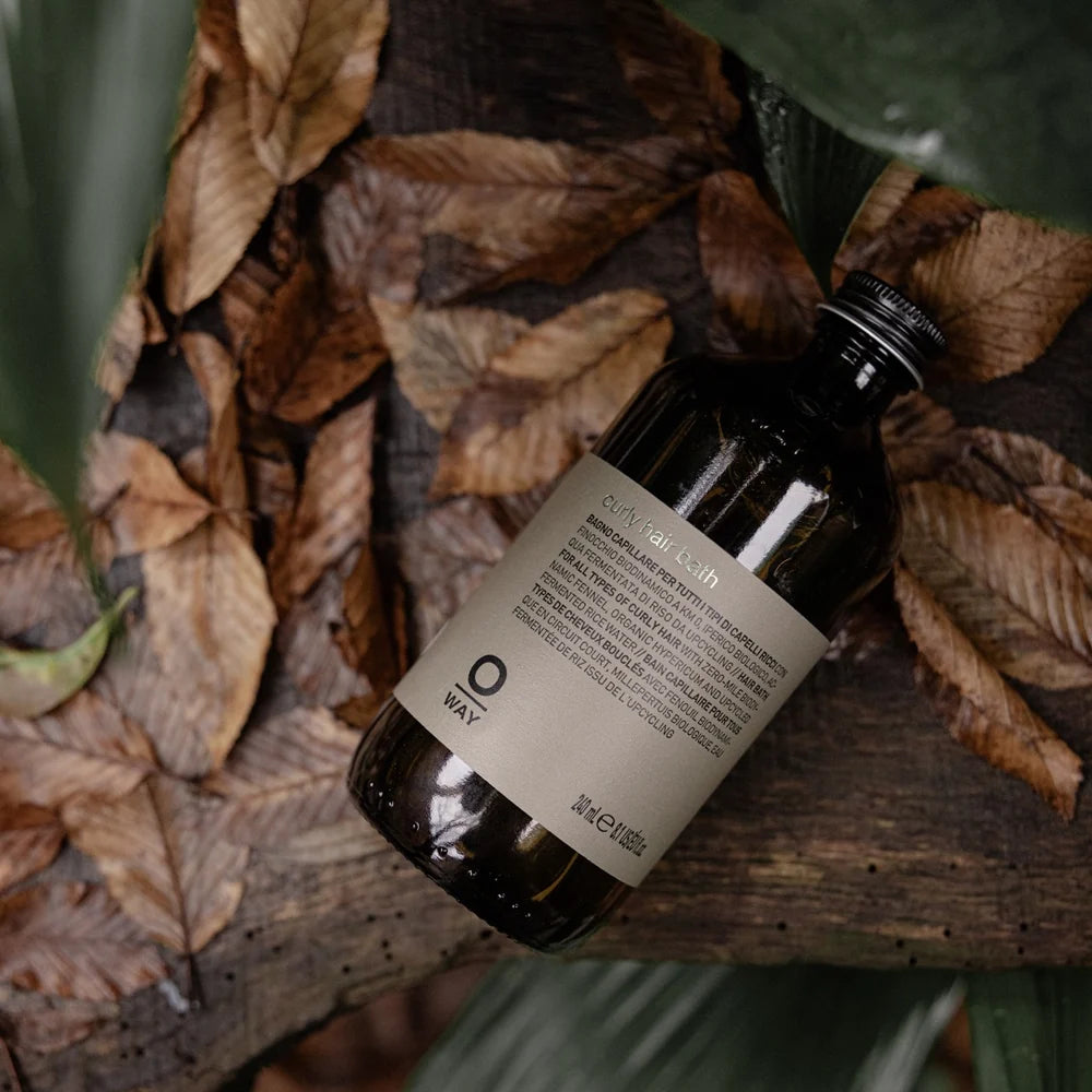 Oway Curly Hair Bath 240ml bottle resting diagonally on bark among dried leaves
