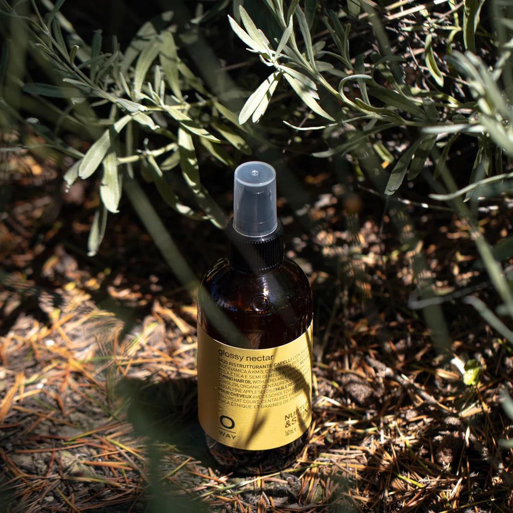 Oway Glossy Nectar bottle standing beneath leafy branches in sunlight