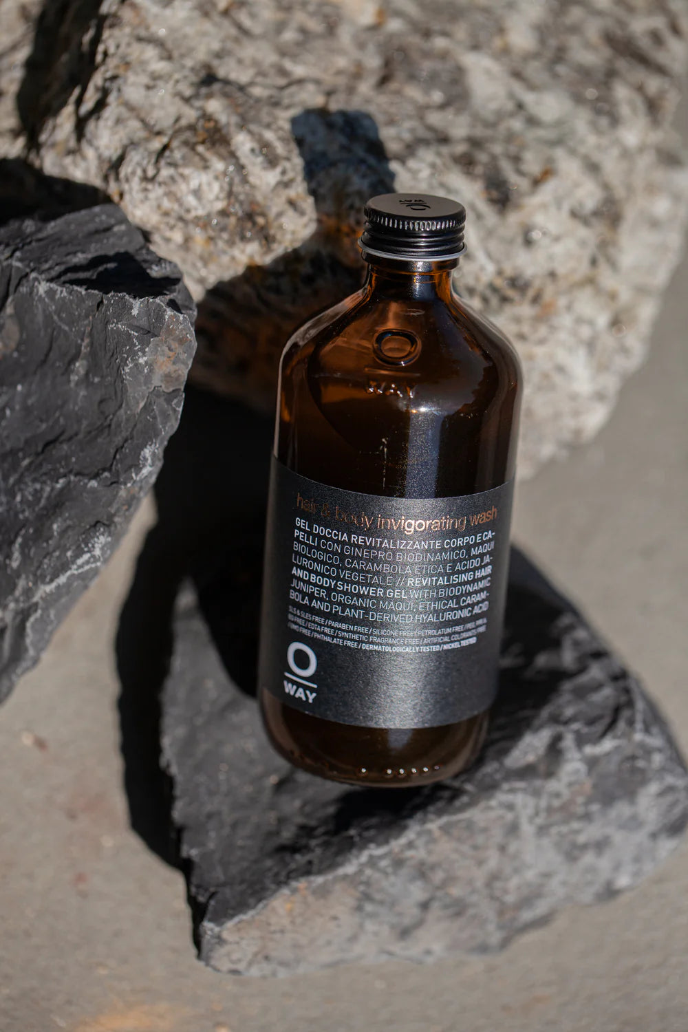 Oway Invigorating Hair & Body Wash bottle nestled between dark and pale rocks