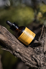 Oway Nurturing Drops bottle resting on a tree branch with foliage in the background