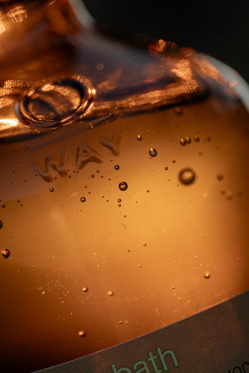 Close-up of the amber glass Oway Purifying Hair Bath bottle with water droplets