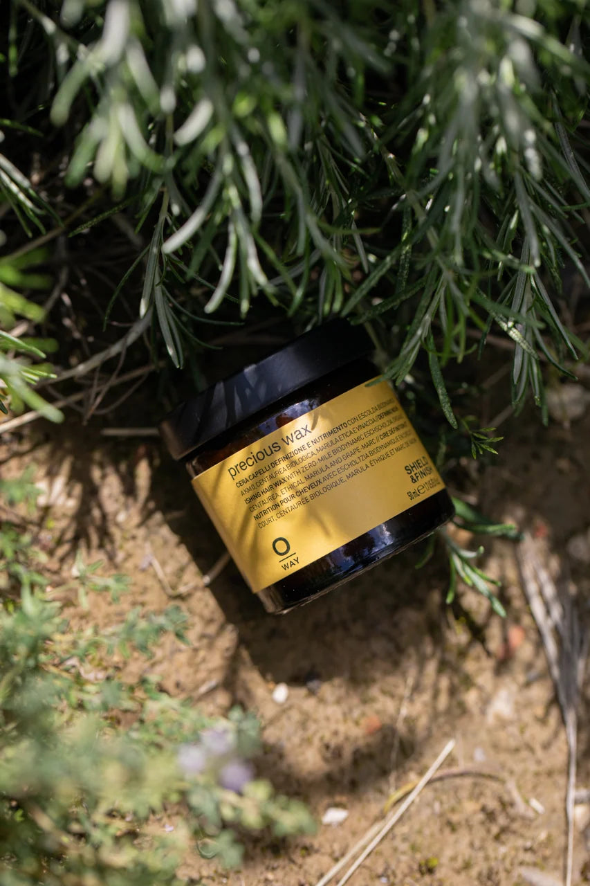 Oway Precious Wax amber glass jar photographed outdoors among green foliage
