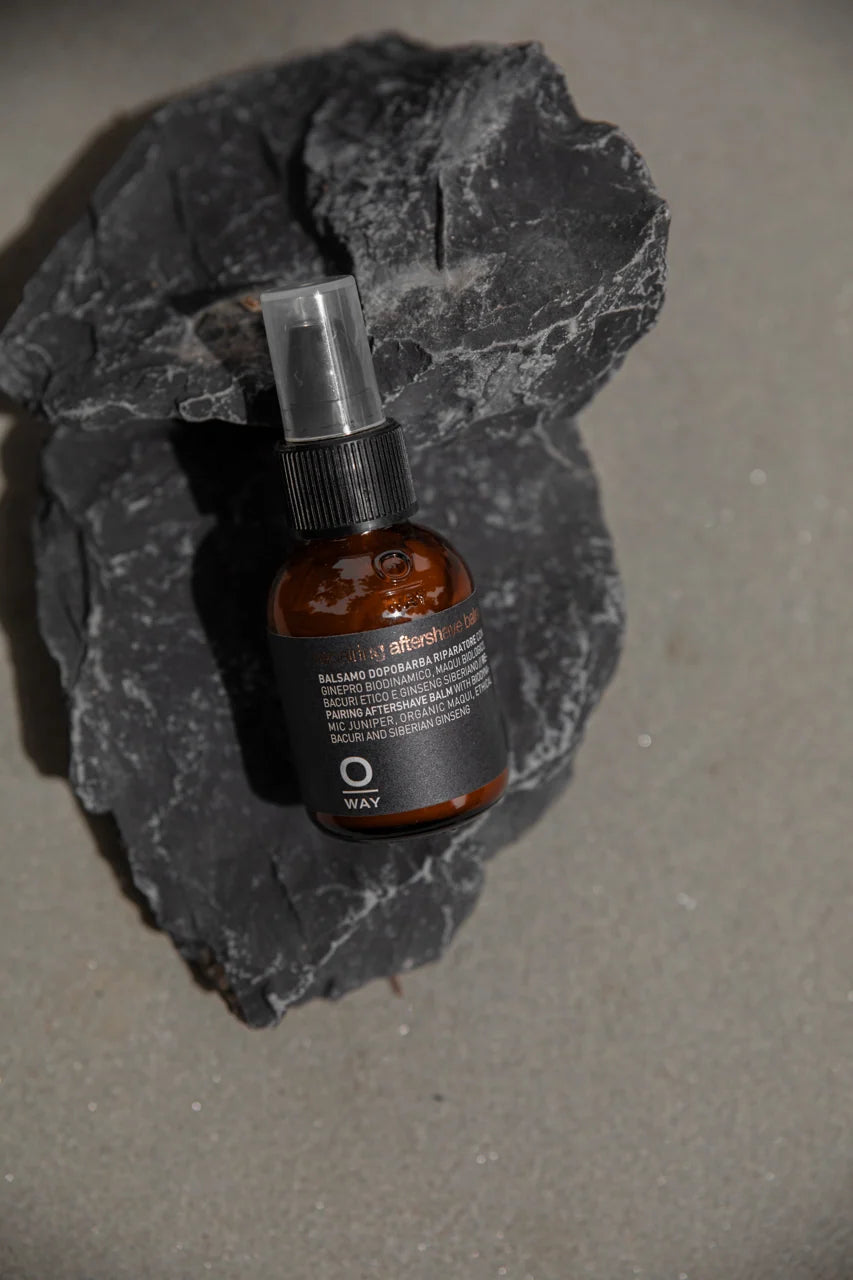 Oway Repairing Aftershave Balm bottle with a clear pump cap resting against dark rocks