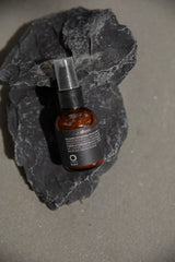 Oway Repairing Aftershave Balm bottle with a clear pump cap resting against dark rocks