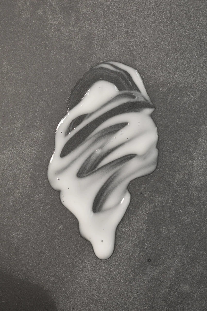 Creamy texture of Oway Sublime Hair Milk 100ml on a dark surface
