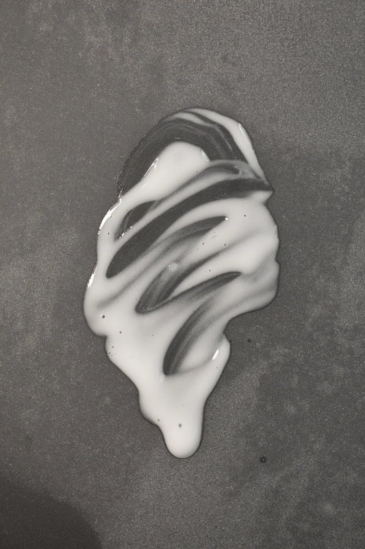 Creamy texture of Oway Sublime Hair Milk 100ml on a dark surface
