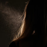 Fine mist being sprayed onto long hair against a dark background