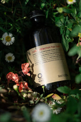 Oway Color Protection Hair Bath bottle among green leaves, white daisies and pink flowers