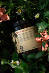 Oway Color Protection Hair Mask jar among green leaves and pink flowers