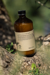 Oway Moisturising Hair Bath 240ml bottle resting against tree bark in sunlight