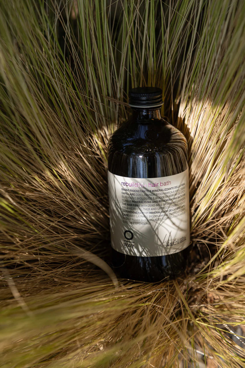 Oway RebuildM+ Hair Bath bottle in a natural botanical setting