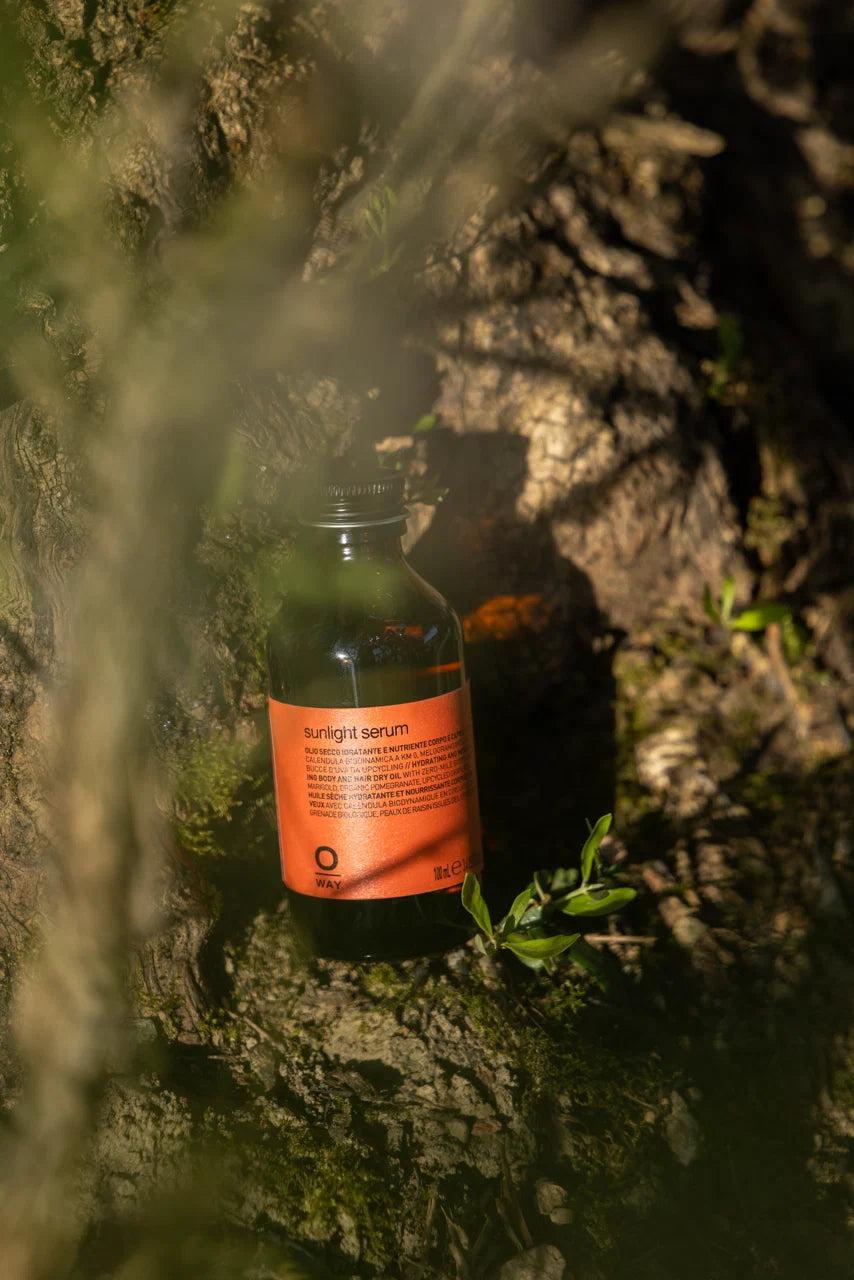 Oway Sunlight Serum amber bottle displayed outdoors against a sunlit tree